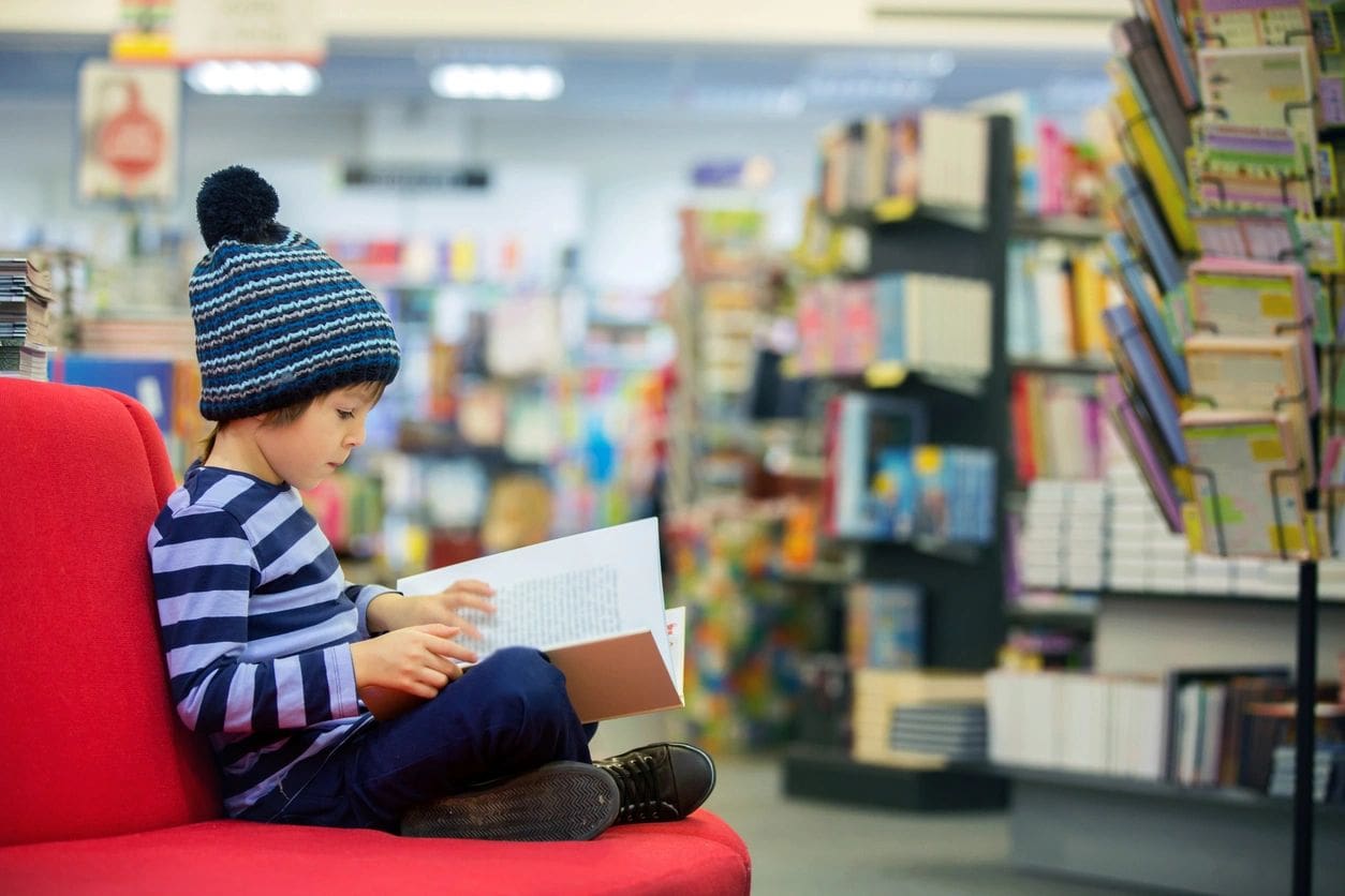 Child reading book on red sofa, bookstore.